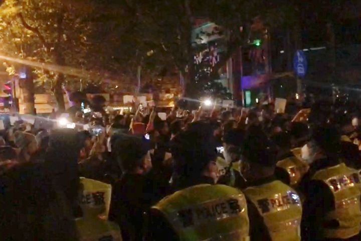 In this image from video obtained by The Associated Press, police, foreground, watch protesters in Shanghai on Saturday, Nov. 26, 2022. Protests against China’s restrictive COVID measures appeared in a number of cities Saturday night, in displays of public defiance fanned by anger over a deadly fire in the western Xinjiang region. (AP Photo)