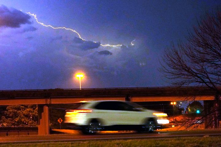 A vehicle races along a Jackson, Miss., street as lightning streaks across the sky, on Nov. 29, 2022. Area residents were provided a light show as severe weather accompanied by some potential twisters affected parts of Louisiana and Mississippi.
