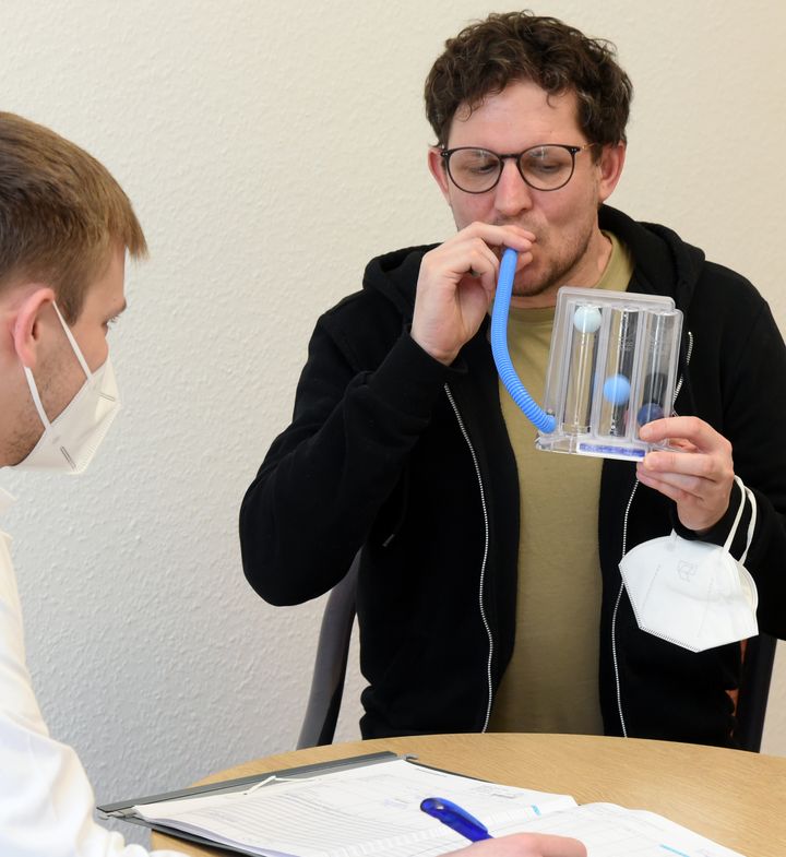 12 Ιανουαρίου 2022, Σαξονία: Στο Haus Herrmannsbad, ο γιατρός ελέγχει τον όγκο των πνευμόνων και την προπόνηση των μυών της εισπνοής με μια συσκευή εκγύμνασης της αναπνοής σε έναν ασθενή με μακροχρόνια συμπτώματα Covid . Η κλινική του Ομίλου Εταιρειών Michels περιθάλπει επί του παρόντος, μαζί με άλλους ασθενείς, άνδρες και γυναίκες που έχουν αναπτύξει μακροχρόνιο σύνδρομο Covid μετά τη νόσο του κορονοϊού. Η αποκατάσταση αποσκοπεί στη μείωση των συνεπειών της νόσου και στην αποκατάσταση της απόδοσης στην εργασία και στην καθημερινή ζωή. (Photo by Waltraud Grubitzsch/picture alliance via Getty Images)