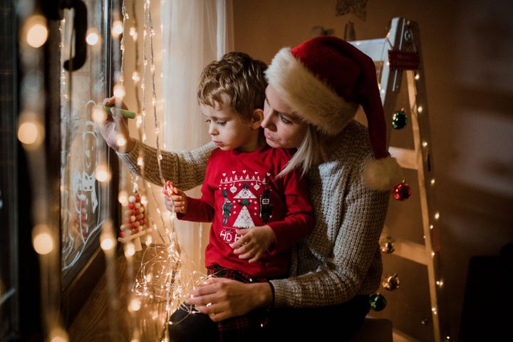 Mother and son draw Christmas holidays decoration painted on window glass.