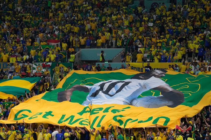 Οι Βραζιλιάνοι οπαδοί κρατούν μια γιγάντια βραζιλιάνικη σημαία με την εικόνα του Πελέ με το μήνυμα που γράφει στα αγγλικά "Πελέ,ταχεία ανάρρωση", κατά τη διάρκεια του αγώνα ποδοσφαίρου του Παγκοσμίου Κυπέλλου μεταξύ Καμερούν και Βραζιλίας, στο στάδιο Lusail στη Λουσαϊλ του Κατάρ, Παρασκευή , 2 Δεκεμβρίου 2022. (AP Photo/Natacha Pisarenko) :