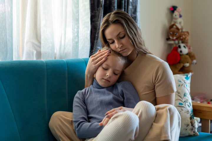 Woman and sad little daughter are sitting on couch and hugging