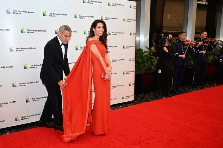 George Clooney adjusts wife Amal's cape on the red carpet.