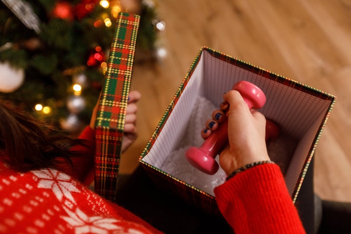 Directly above shot of unrecognizable woman sitting by the Christmas tree and taking a dumbbell out of a Christmas gift box that she opened.