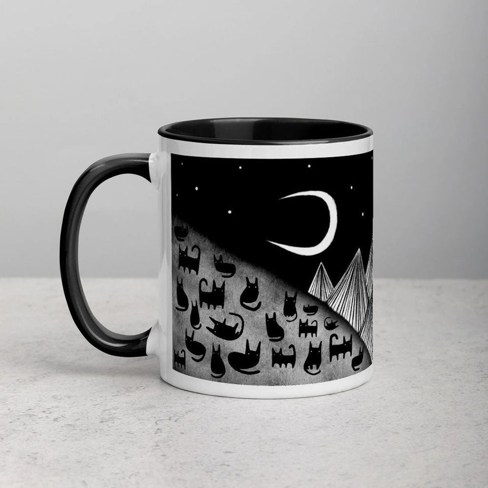 A cute and quirky ceramic mug featuring black cats looking up at a crescent moon