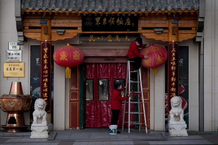A masked worker on a ladder cleans a dusty lantern outside a steamboat restaurant at the Wangfujing shopping district in Beijing, on Dec. 14, 2022. China's National Health Commission scaled down its daily COVID-19 report starting Wednesday in response to a sharp decline in PCR testing since the government eased anti-virus measures and daily cases hit record highs.