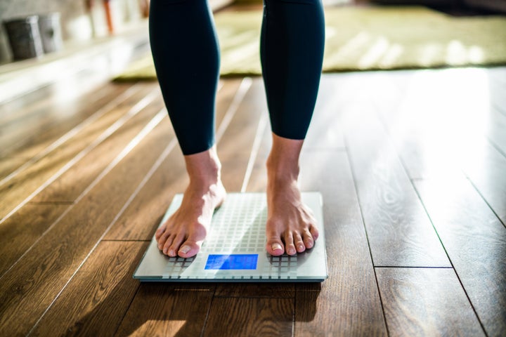 Low section of woman checking her weight on the scale at home