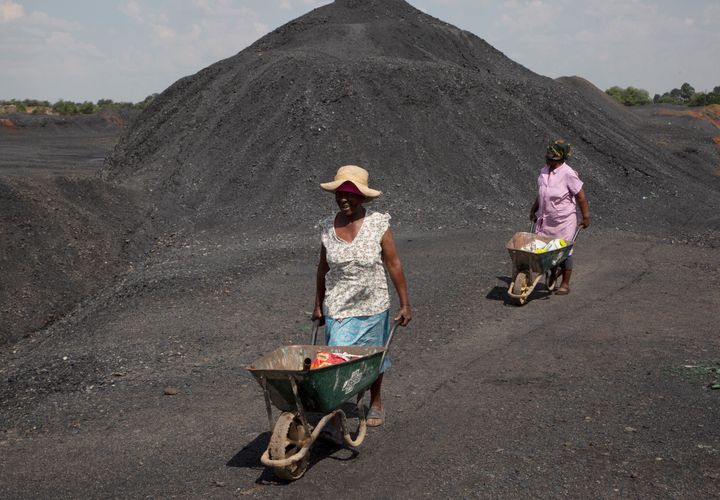 Γυναίκες από την πόλη Masakhane, σπρώχνουν καροτσάκια πάνω από μια χωματερή ανθρακωρυχείου στον ηλεκτροπαραγωγικό σταθμό Duvha που λειτουργεί με άνθρακα, κοντά στο Emalahleni (πρώην Witbank) ανατολικά του Γιοχάνεσμπουργκ, Πέμπτη, 17 Νοεμβρίου 2022. Ζώντας στη σκιά ενός από τους μεγαλύτερους σταθμούς ηλεκτροπαραγωγής της Νότιας Αφρικής με καύση άνθρακα, οι κάτοικοι του Μασαχάνε φοβούνται απώλεια θέσεων εργασίας εάν κλείσει η εγκατάσταση καθώς η χώρα κινείται προς καθαρότερη ενέργεια. Σημαντικός παράγων ρύπανσης της ατμόσφαιρας, επειδή βασίζεται στον άνθρακα για να παράγει περίπου το 80% της ηλεκτρικής της ενέργειας, η Νότια Αφρική σχεδιάζει να μειώσει τη χρήση άνθρακα στο 59% έως το 2030, καταργώντας ορισμένους από τους 15 σταθμούς ηλεκτροπαραγωγής με καύση άνθρακα και αυξάνοντας τη χρήση ανανεώσιμων πηγών ενέργειας. (AP Photo/Denis Farrell)