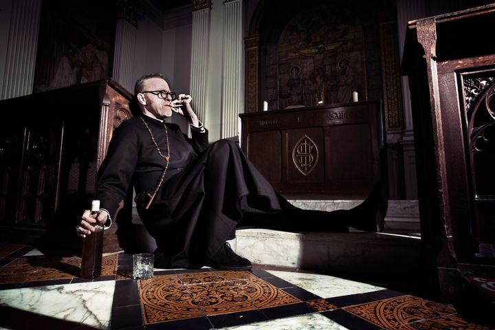 A priest takes time out to contemplate life with a smoke and a whisky.