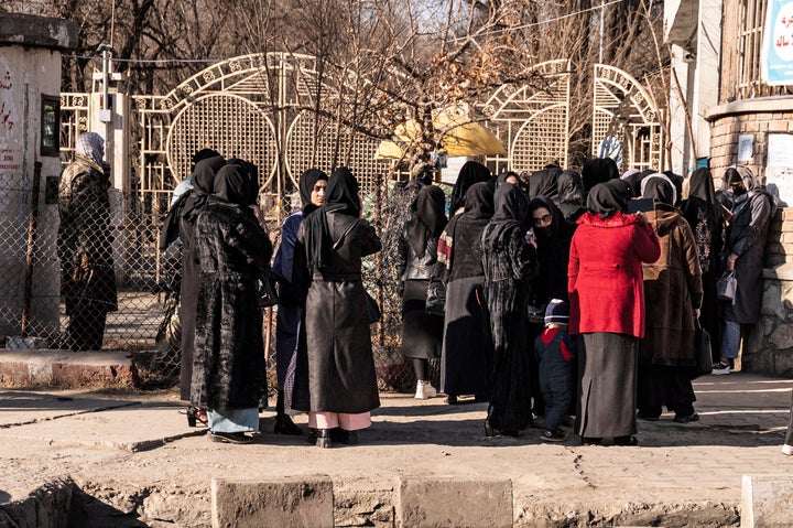 Afghan female university students stop by Taliban security personnel stand next to a university in Kabul on Dec. 21, 2022.