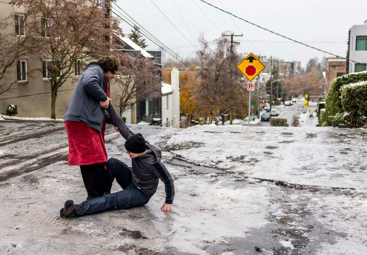 CORRECTS PHOTOGRAPHERS NAME - Garrett Fuller, left, helps friend Robin Jacobs get up after slipping to the icy ground on Capitol Hill, Friday, Dec. 23, 2022 in Seattle. Winter weather is blanketing the U.S. as a massive storm sent temperatures crashing and created whiteout conditions. (Daniel Kim/The Seattle Times via AP)