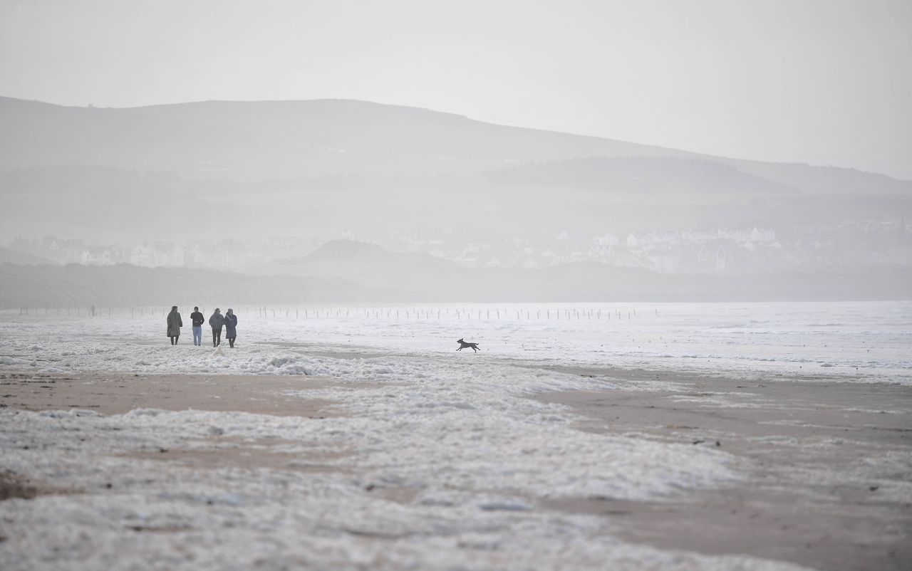 People walking through the sea foam that gathered on the beach at Portstewart, Northern Ireland, as a result of Storm Franklin on February 21, 2022.