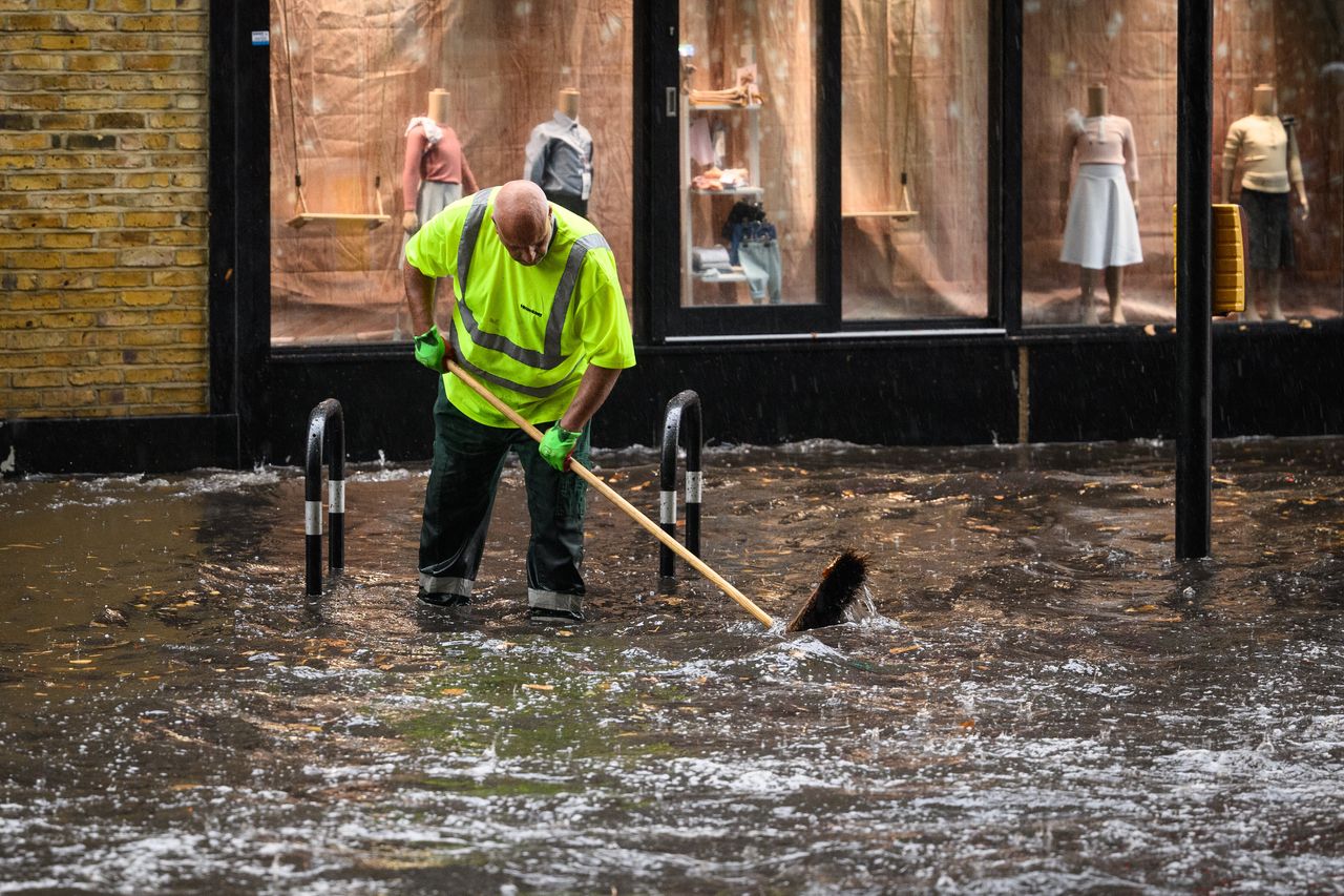 A council worker attempts to clear a drain with his broom, as torrential rain and thunderstorms hit the South East on August 17, 2022