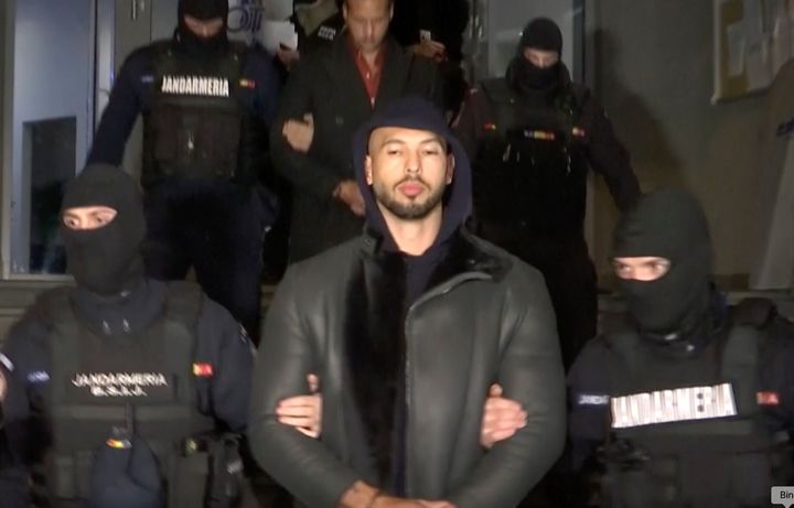 In an image from a video released by Observator Antena 1, social media personality Andrew Tate is led away by police Thursday in the Ilfov area north of Bucharest, Romania.