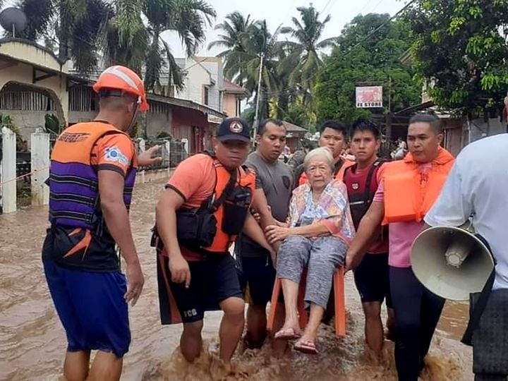 In this image provided by the Philippine Coast Guard, an elderly woman sits on a chair while being carried by coast guard personnel wading through floodwaters in Plaridel, Misamis Occidental province in the southern Philippines, Monday, Dec. 26, 2022. Heavy rains and floods devastated parts of the Philippines over the Christmas weekend. (Philippine Coast Guard via AP)