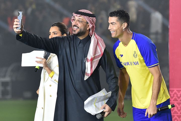TOPSHOT - Al-Nassr's new Portuguese forward Cristiano Ronaldo (R), wearing a cross earing, poses for a selfie with the presenters during his unveiling at the Mrsool Park Stadium in the Saudi capital Riyadh on January 3, 2023. (Photo by AFP) (Photo by -/AFP via Getty Images)
