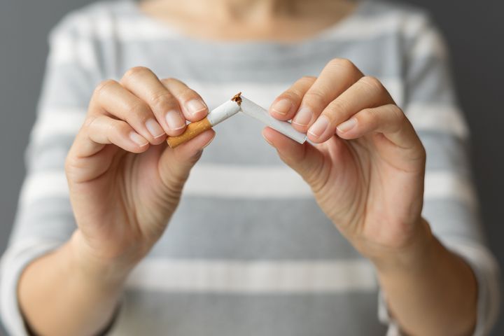 Close up young woman holding broken cigarette in hands. Happy female quitting refusing smoking cigarettes. Quit bad habit, Stop smoking cigarettes, health care concept. No smoking campaign.