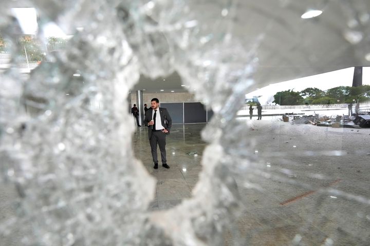 A worker stands on the other side of a broken window at Planalto Palace the day after the office of the president was stormed by supporters of Brazil's former President Jair Bolsonaro in Brasilia, Brazil, on Jan. 9, 2023. 