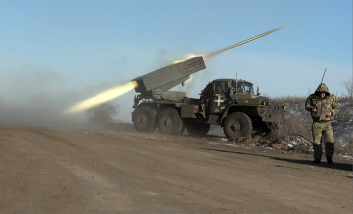 A member of Ukraine's military looking away as a rocket launcher fires on the outskirts of Soledar.