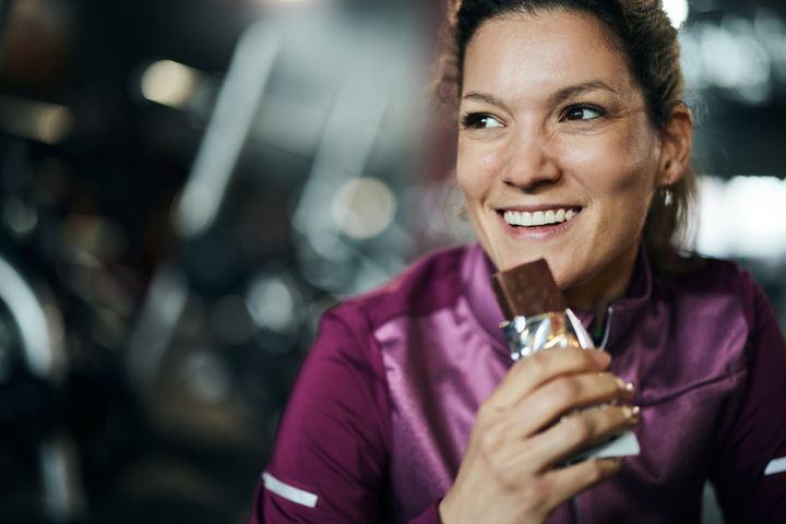 Happy woman eating protein bar on a break from sports training.