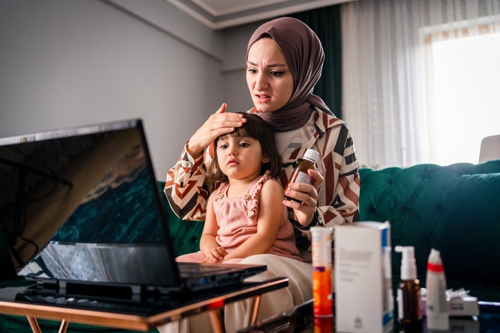 mother having video call with a pediatrician while holding ill daughter in her lap.