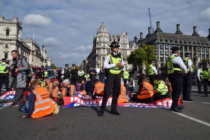 Police guard activists sitting with their hands glued to the road and holding Insulate Britain banners in Parliament Square.