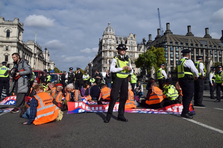 Police guard activists sitting with their hands glued to the road and holding Insulate Britain banners in Parliament Square.