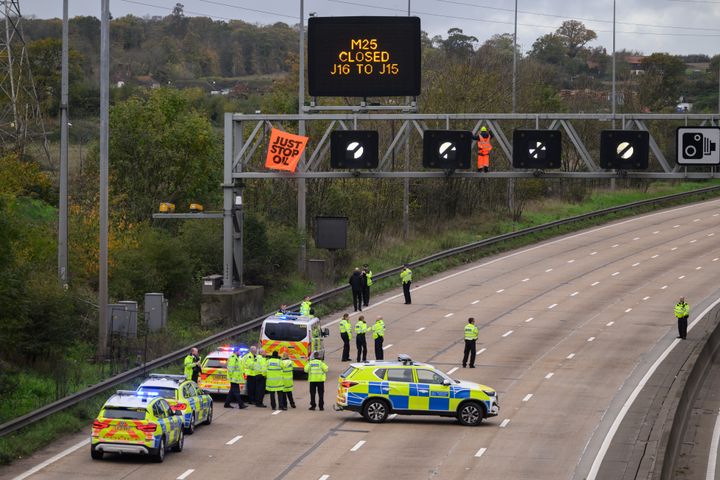 Police officers attempt to stop an activist as they put up a banner reading "Just Stop Oil" atop an electronic traffic sign along M25.