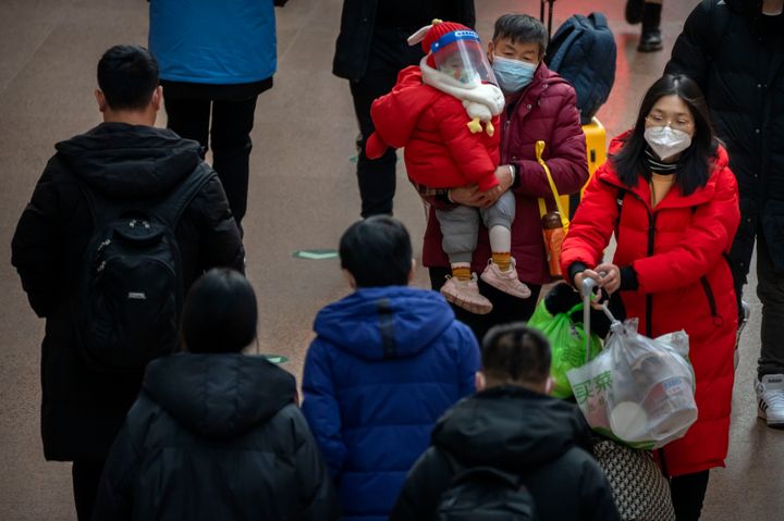 A woman carries a child wearing a face mask and face shield as they walk along a concourse at Beijing West Railway Station in Beijing, on Jan. 18, 2023.