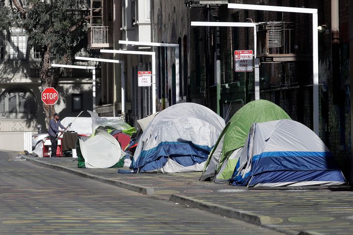 A man stands next to tents on a sidewalk in San Francisco. 