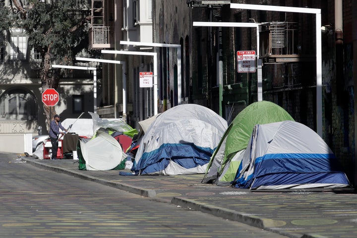 A man stands next to tents on a sidewalk in San Francisco.