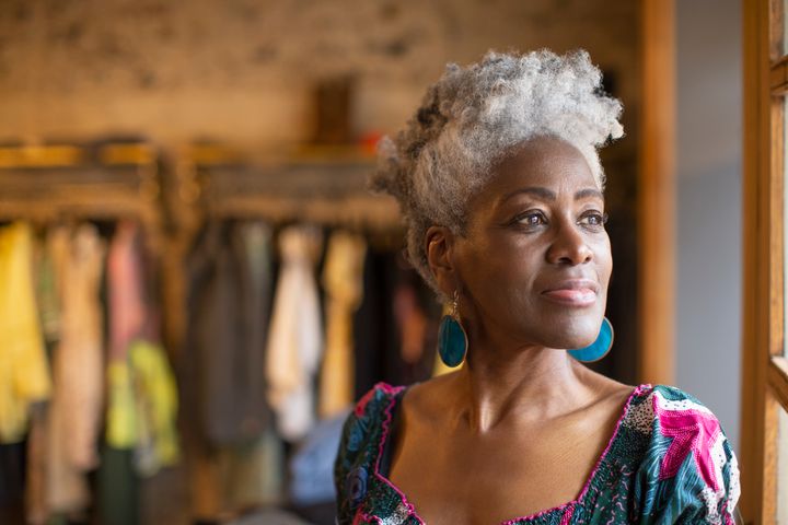 Portrait thoughtful senior female shop owner with gray hair looking out boutique window