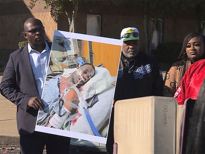 In this photo provided by WREG, Tyre Nichols' stepfather, Rodney Wells, center, stands next to a photo of Nichols in the hospital after his arrest. The photo was shown at a Memphis, Tennessee protest on Jan. 14.