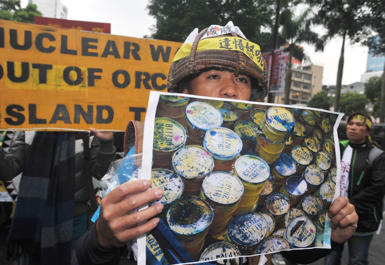 A protester in traditional Tao dress at a March 2021 anti-nuclear rally in Taipei holds a picture of low-radiation nuclear waste being stored on remote Orchid Island.