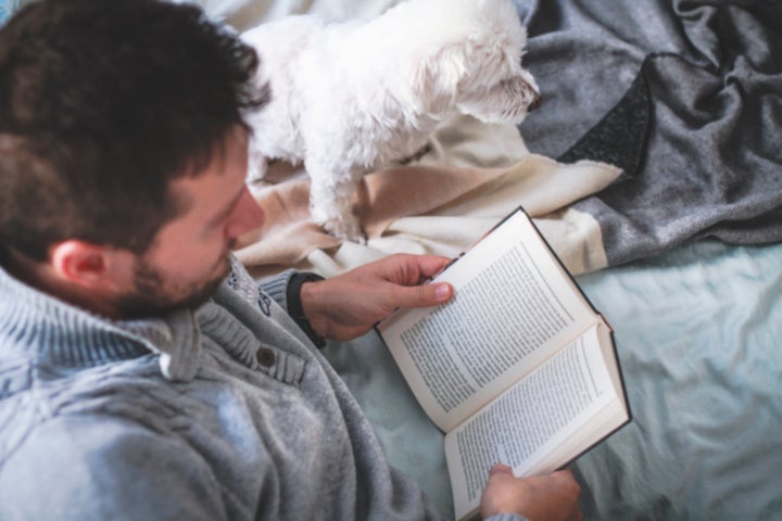 Man reading book in the bed, cuddling with his dog. Top view. Insomnia. Winter morning