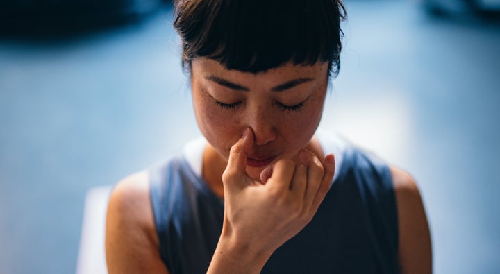 Low angle view of happy Asian woman in sportswear doing alternative nostril breathing exercise in the yoga studio.