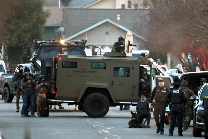Law enforcement officers aim their weapons at a home during a standoff in Grants Pass, Ore., on Tuesday, Jan. 31, 2023. Police said the standoff involving a man suspected in a violent kidnapping in Oregon who was barricaded underneath the home has been “resolved.”