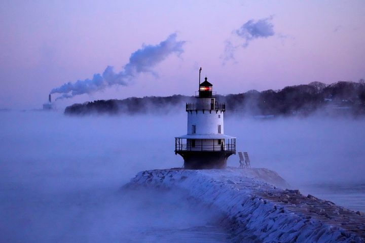 Spring Point Ledge Light is surrounded by arctic sea smoke while emissions from the Wyman Power plant, background, are blown horizontal by the fierce wind, Saturday, Feb. 4, 2023, in South Portland, Maine.