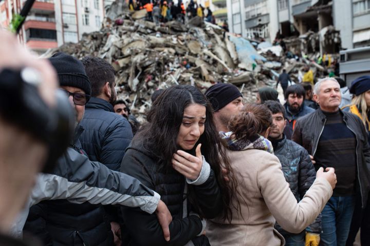 トルコ・アダナで倒壊した建物の瓦礫の中から生存者を探す救助隊と女性