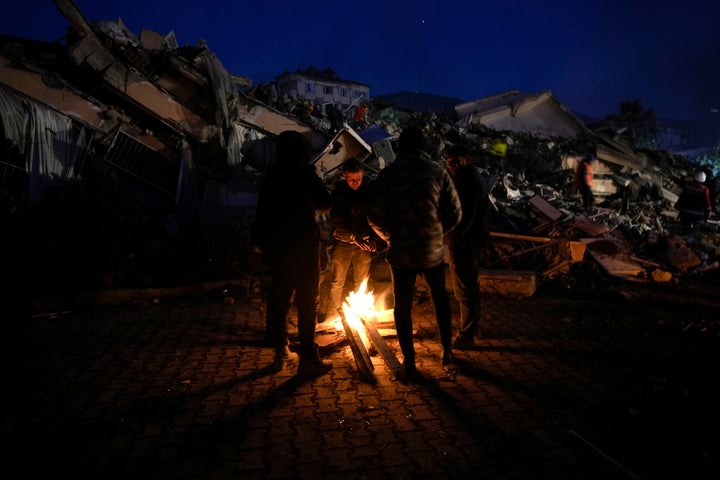 People warm up with fire in front of destroyed buildings in Antakya, southern Turkey, on Feb. 8, 2023.