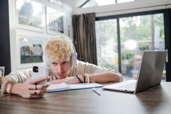 Young blonde man having a break from work at home. He is looking at the phone.