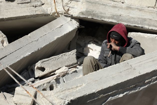 がれきの上に座り、倒壊した建物の下に閉じ込められた家族の情報を待つシリアの男性（2023年2月8日）