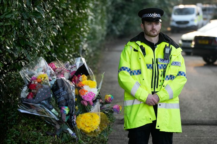 A police officer stands next to floral tributes at the entrance to Linear Park where 16-year-old Brianna Ghey was found with multiple stab wounds on a path in Culcheth on Saturday on February 13, 2023
