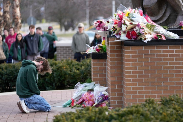 A student kneels where flowers are being left at the Spartan Statue on the grounds of Michigan State University, in East Lansing, Mich., on, Feb. 14, 2023.