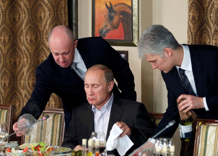 Evgeny Prigozhin assists Russian Prime Minister Vladimir Putin during a dinner with foreign scholars and journalists in 2011