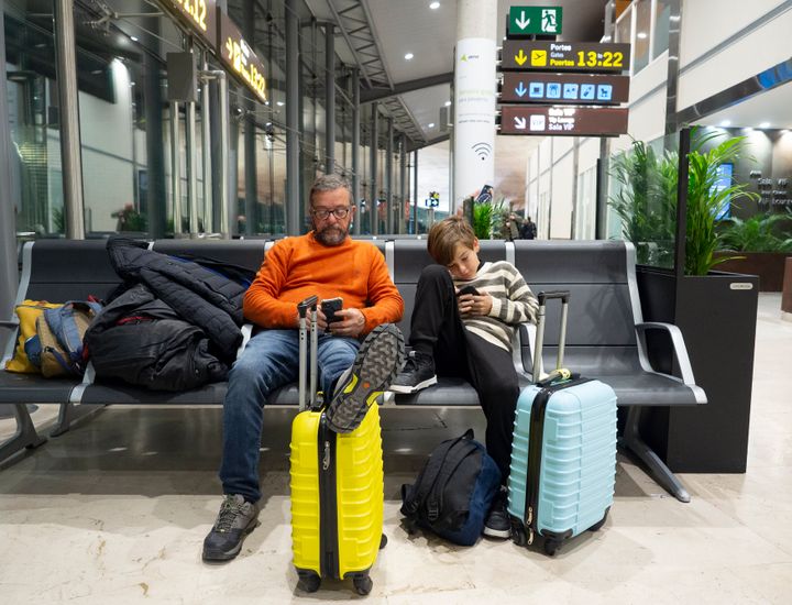 Father and son sitting on a bench using a mobile phone while waiting for flight at the airport lounge
