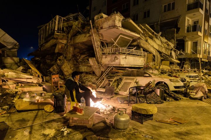 Ένας άνδρας μιλάει στο τηλέφωνο καθώς κάθεται δίπλα σε μια πυρκαγιά κοντά σε ένα κατεστραμμένο κτίριο στον απόηχο ενός θανατηφόρου σεισμού στην Aντάκια της Τουρκίας, στις 20 Φεβρουαρίου 2023.