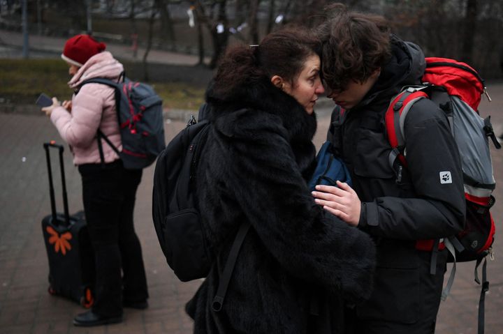 People hug as a woman with a suitcase uses her smartphone outside a metro station in Kyiv in the morning of February 24, 2022.