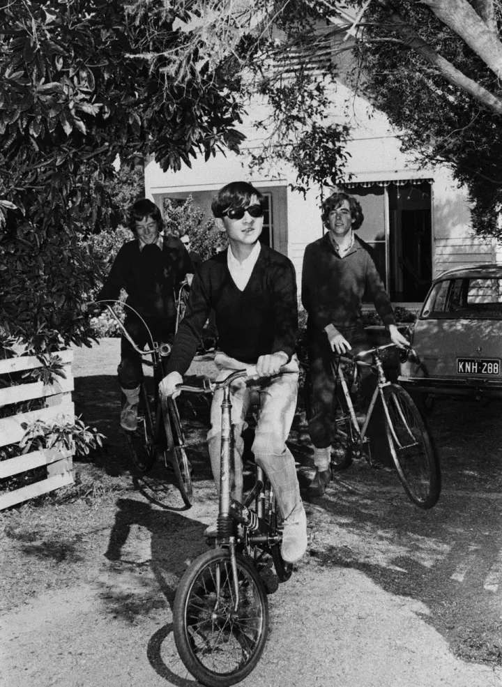 メルボルンの郊外ポイントロンズデールにあるコリン・ハーパー夫妻の別荘で、自転車に乗り門を出る浩宮さま。左はホストのハーパー家のアレックス君、右はアダム君＝1974年8月23日、オーストラリア・ポイントロンズデール