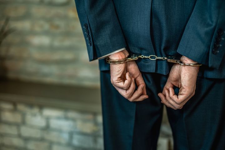 Hand close-up of unrecognizable businessman in handcuffs getting arrested.